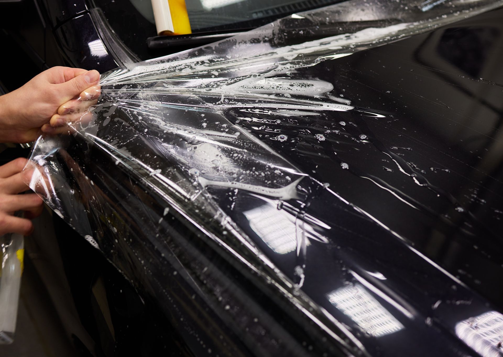 Hands applying clear film to a glossy black car hood