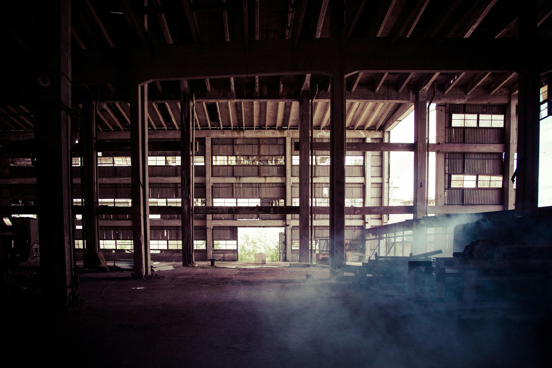Interior of abandoned building with visible support beams, windows, and hazy atmosphere.
