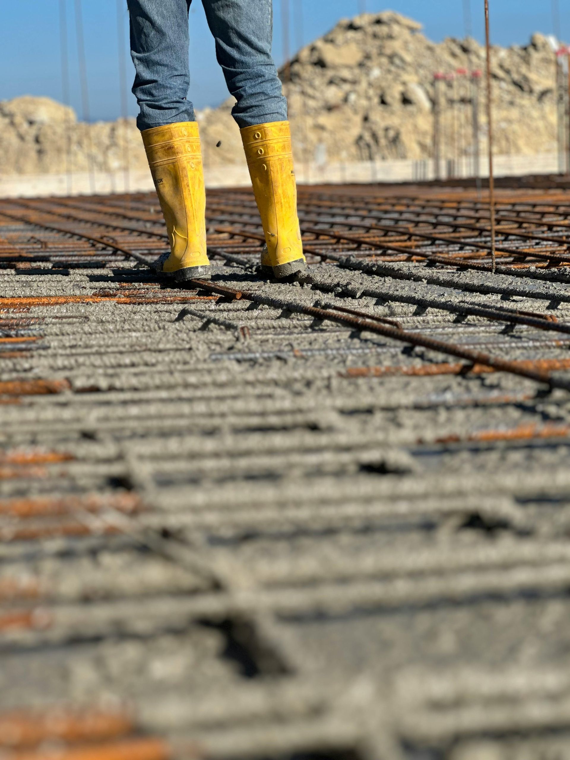 Person in yellow boots stands on a construction site with exposed rebar.