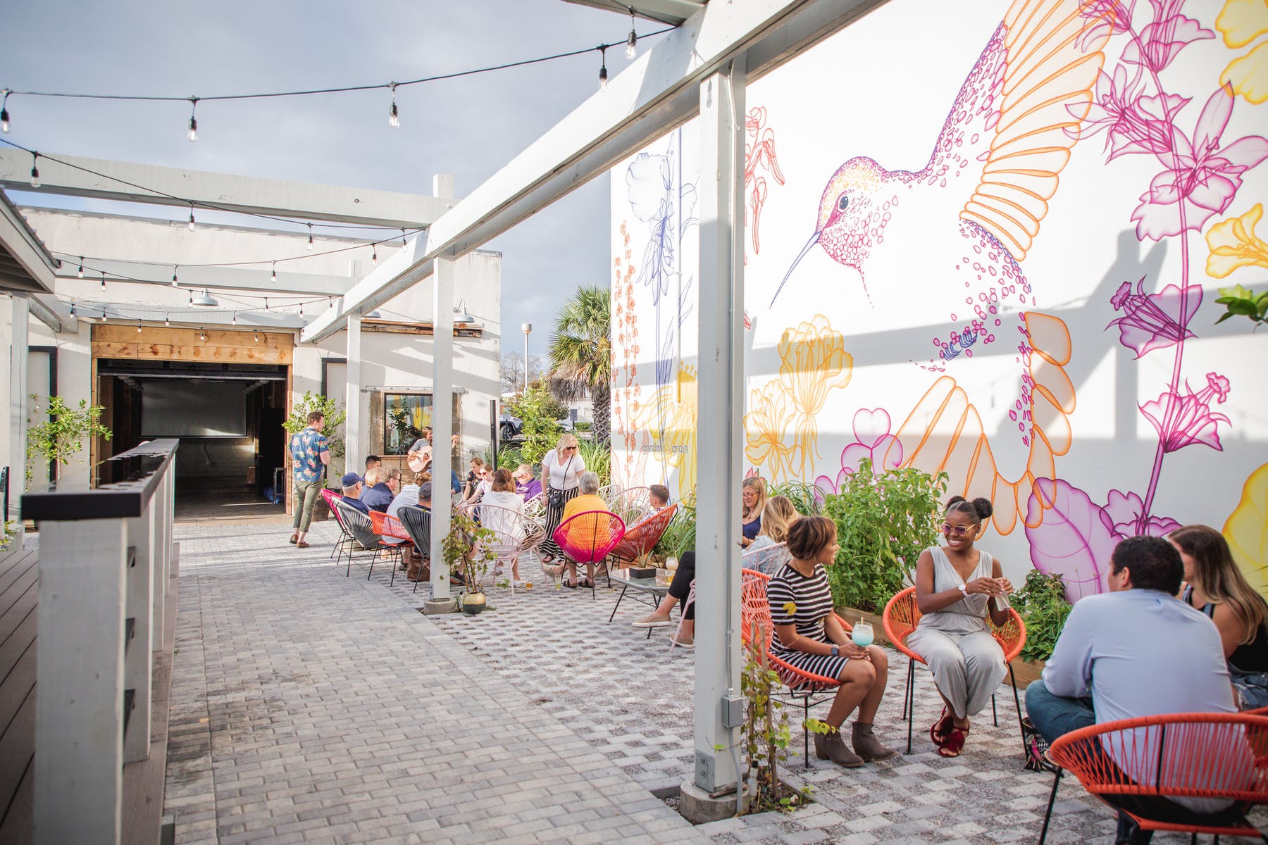 A group of people are sitting under a covered area with a mural on the wall