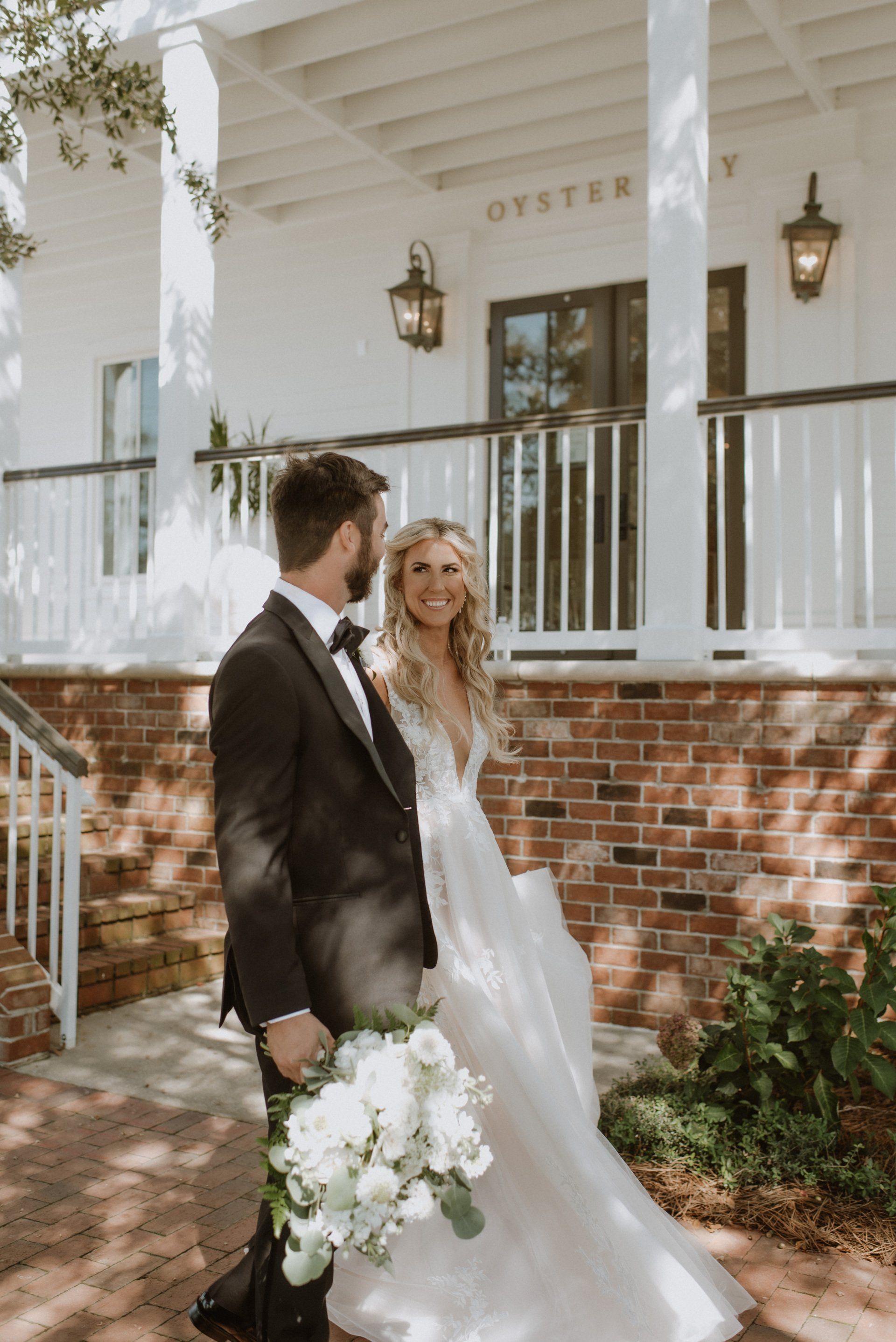 A bride and groom are standing in front of a building with a brick base that says oyster bay