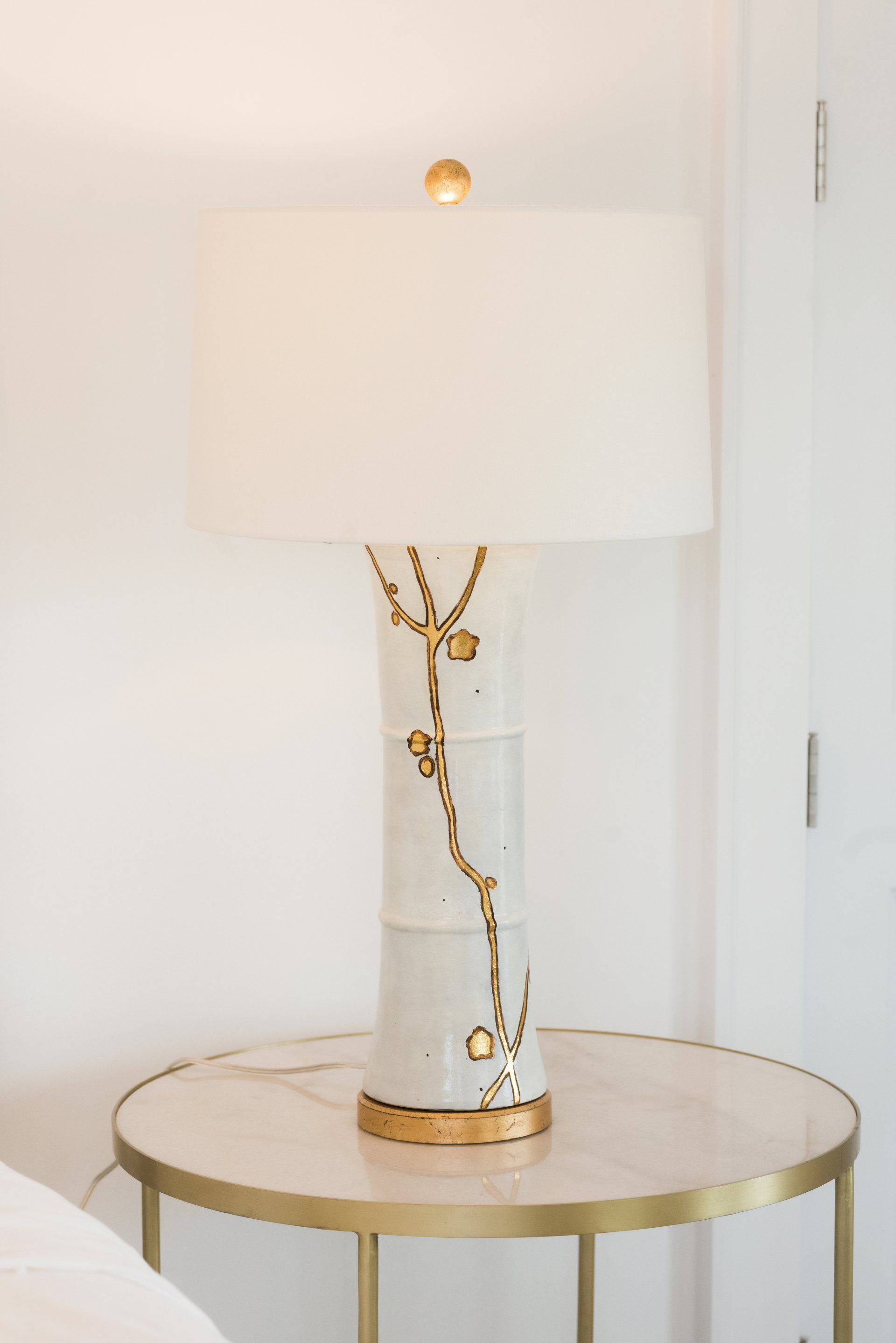 A white lamp with a gold base sits on a table