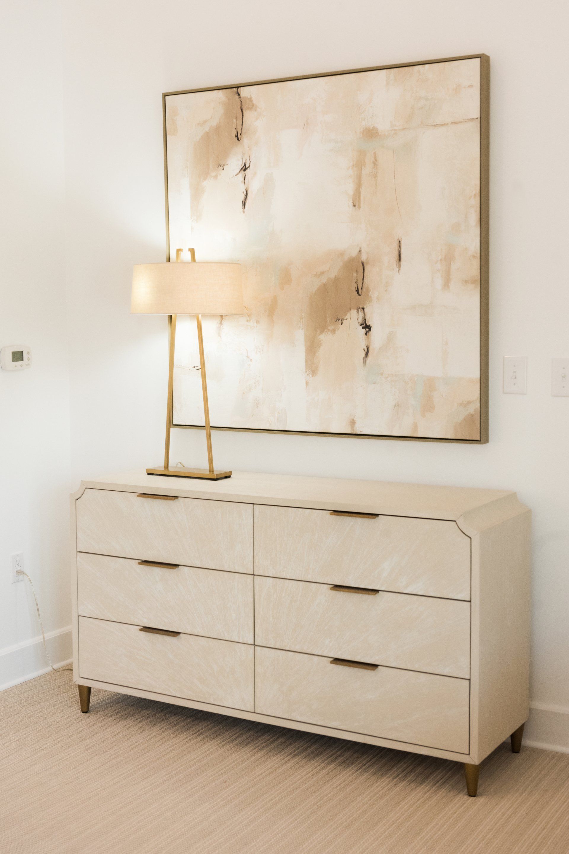 A dresser with a lamp and a painting on the wall above it in an oyster bay boutique hotel room