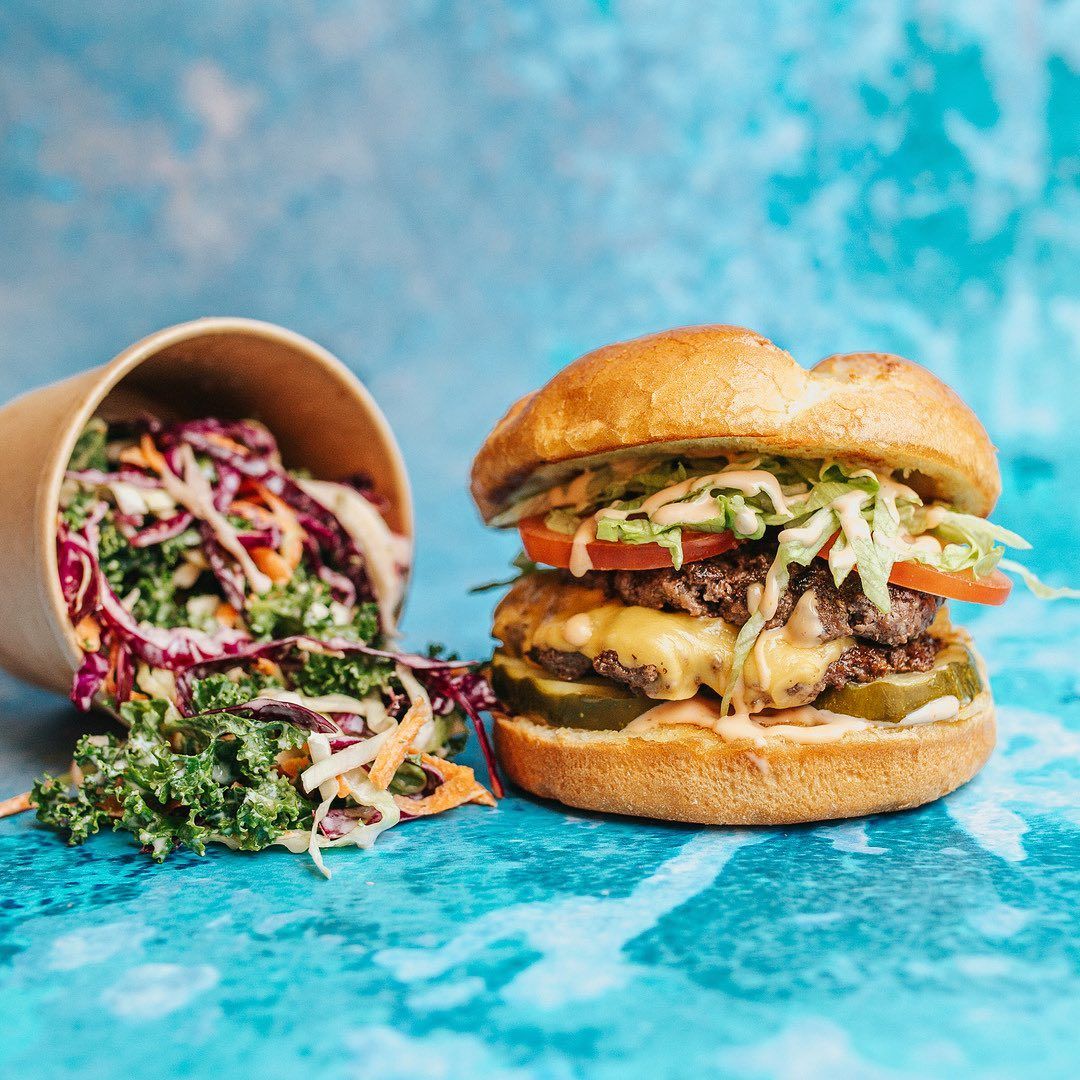 A hamburger next to a cup of coleslaw on a table