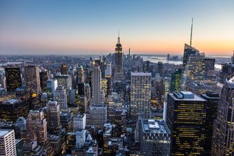 New York City skyline at dusk with lit skyscrapers and a pastel sunset sky