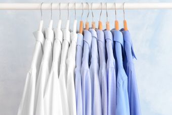 White and light blue button-up shirts hanging neatly on wooden hangers against a soft blue background