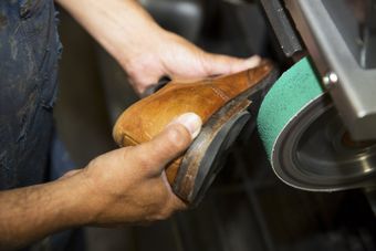 Hands sanding a wooden shoe on a belt sander in a workshop