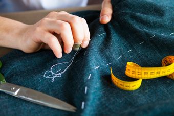 Hands marking fabric with tailor’s chalk beside a yellow measuring tape and scissors