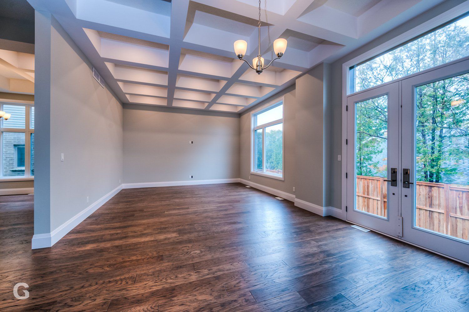 An empty living room with hardwood floors and a chandelier.