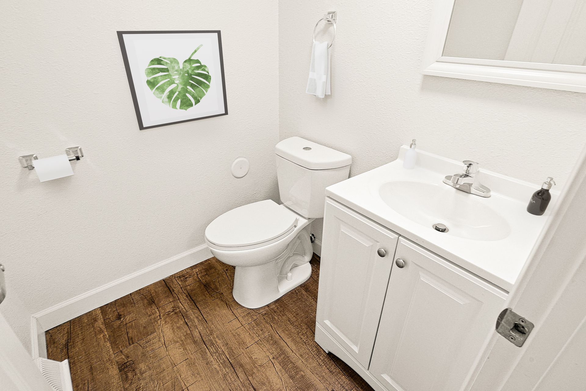 Small bathroom with toilet, sink vanity, wood-look floor, and leaf wall art.