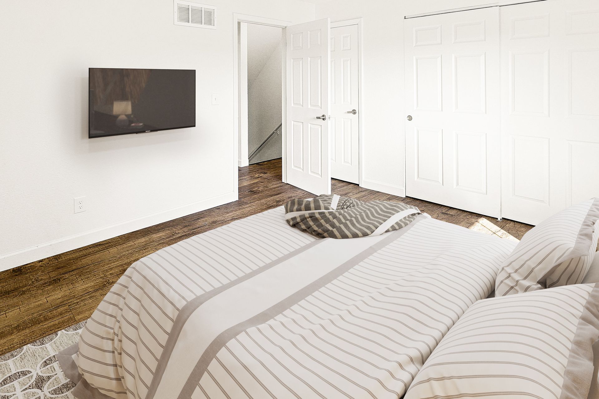Bright bedroom with white walls, striped bedspread, wall-mounted TV, and open closet doors