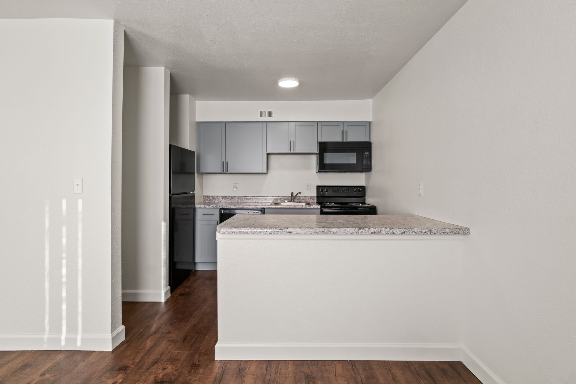 Small modern kitchen with white cabinets, black appliances, and a granite breakfast bar opening to a wood floor.