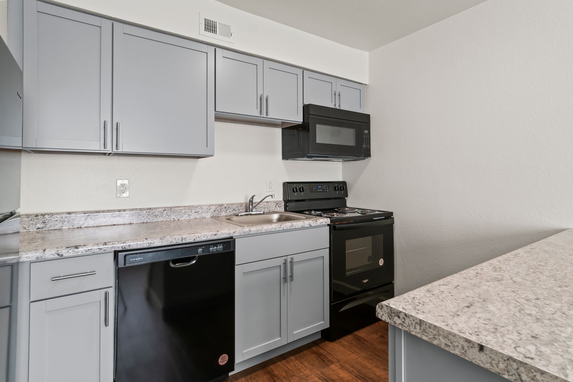 Modern kitchen with gray cabinets, black appliances, and speckled granite countertops