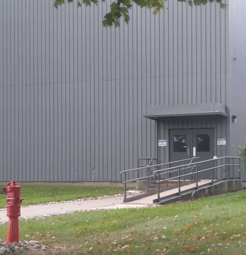 Exterior of a gray industrial building with a ramp leading to double doors. A red fire hydrant is in the foreground.