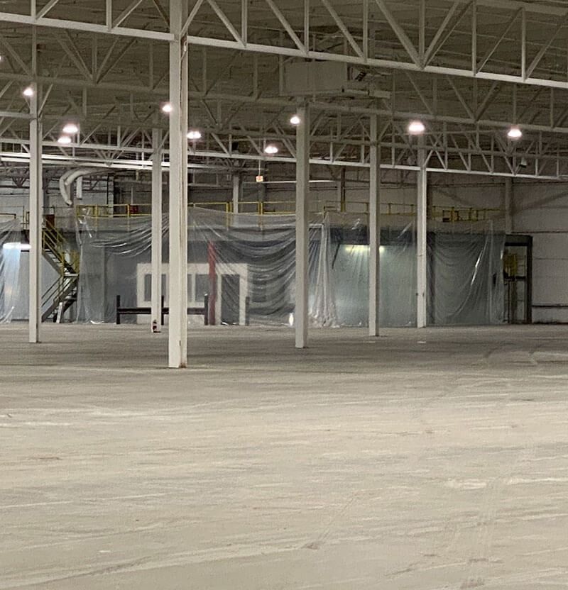 An empty industrial warehouse with tall white support beams and a concrete floor.