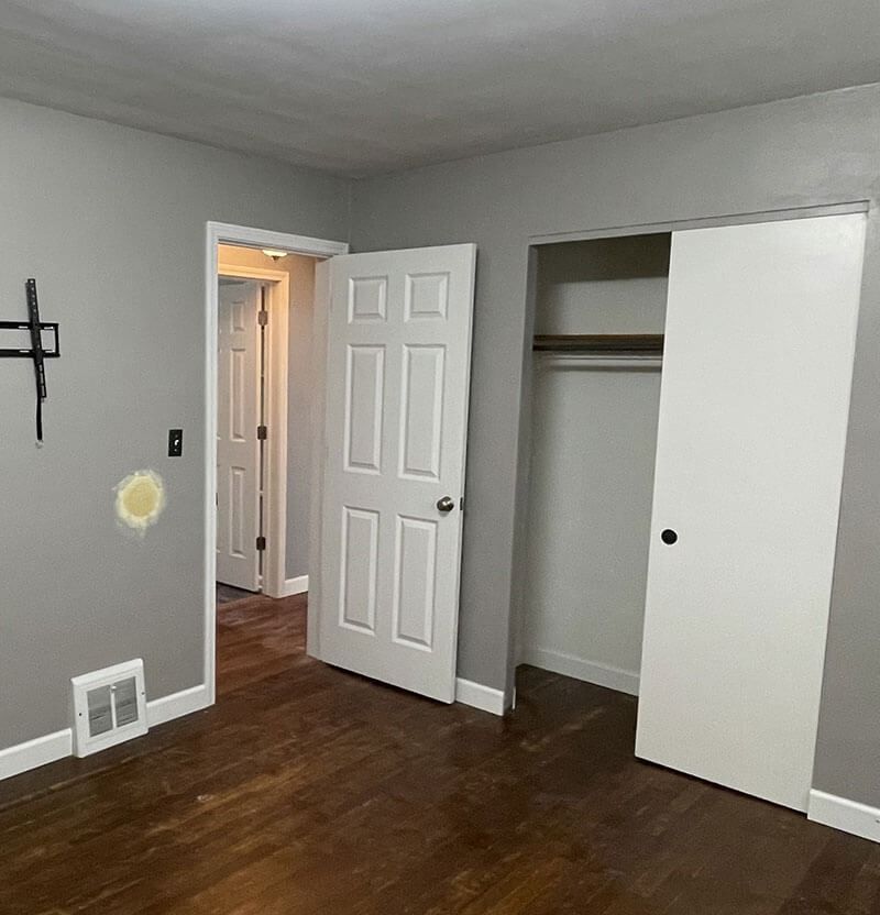 Bedroom with gray walls, dark wood floor, white doors, and a closet.