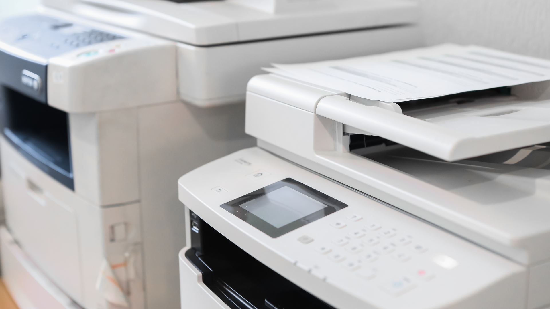 Two copiers are sitting next to each other in a room.