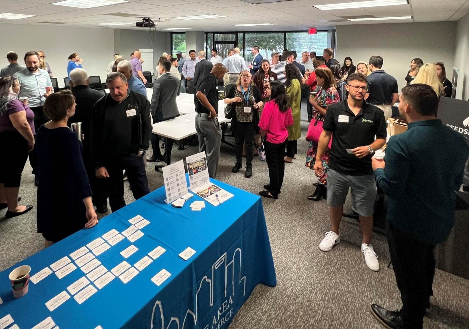 People gathered at a networking event around a blue table with name cards and brochures in a conference room.