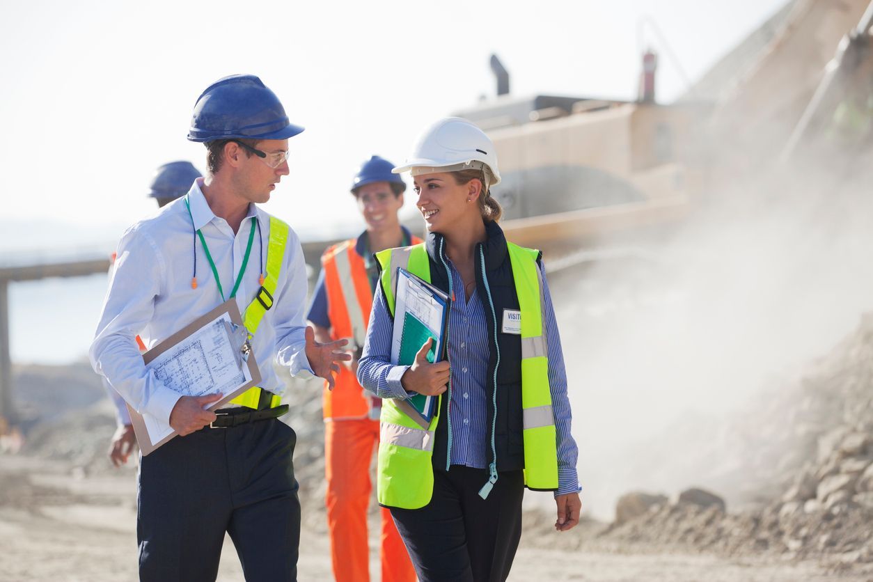 A group of construction workers are walking down a dirt road and talking to each other.