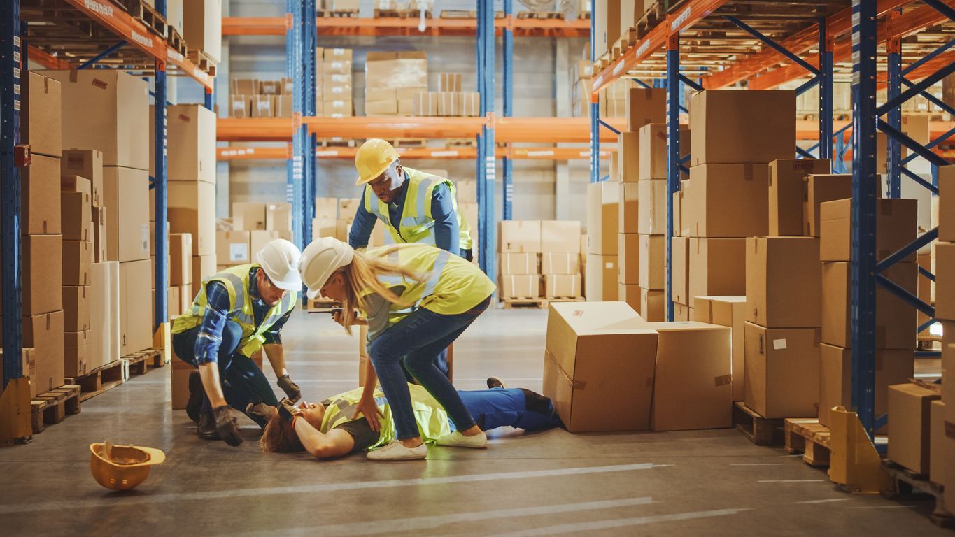 A group of construction workers are helping a man who has fallen in a warehouse.