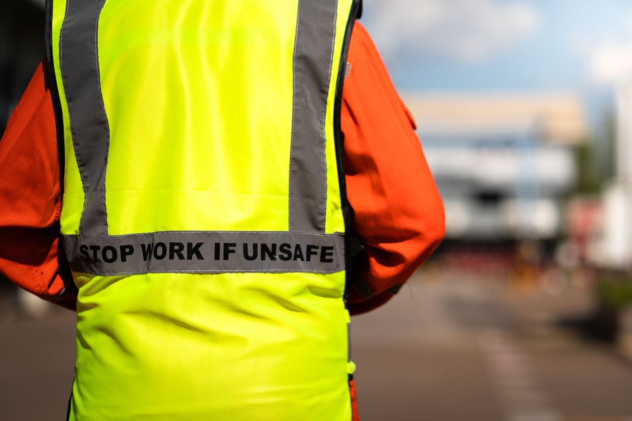Construction worker in a neon yellow safety vest with “STOP WORK IF UNSAFE” on a blurred roadside background