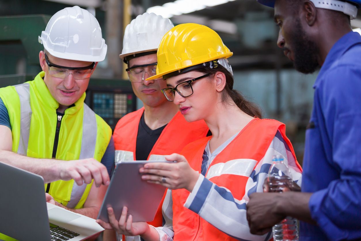 Workers in hard hats and safety vests reviewing plans on a tablet at a job site