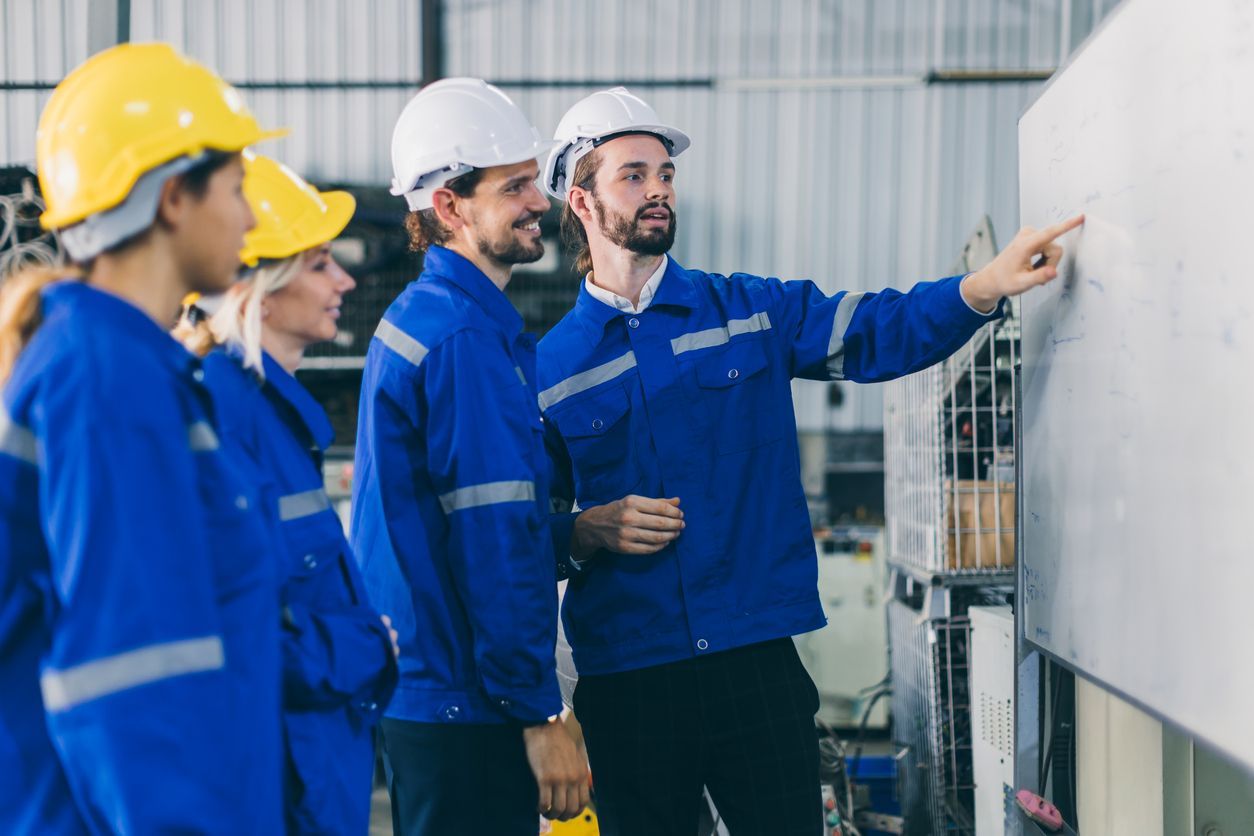 Workers in blue safety uniforms and hard hats inspecting a machine in an industrial facility
