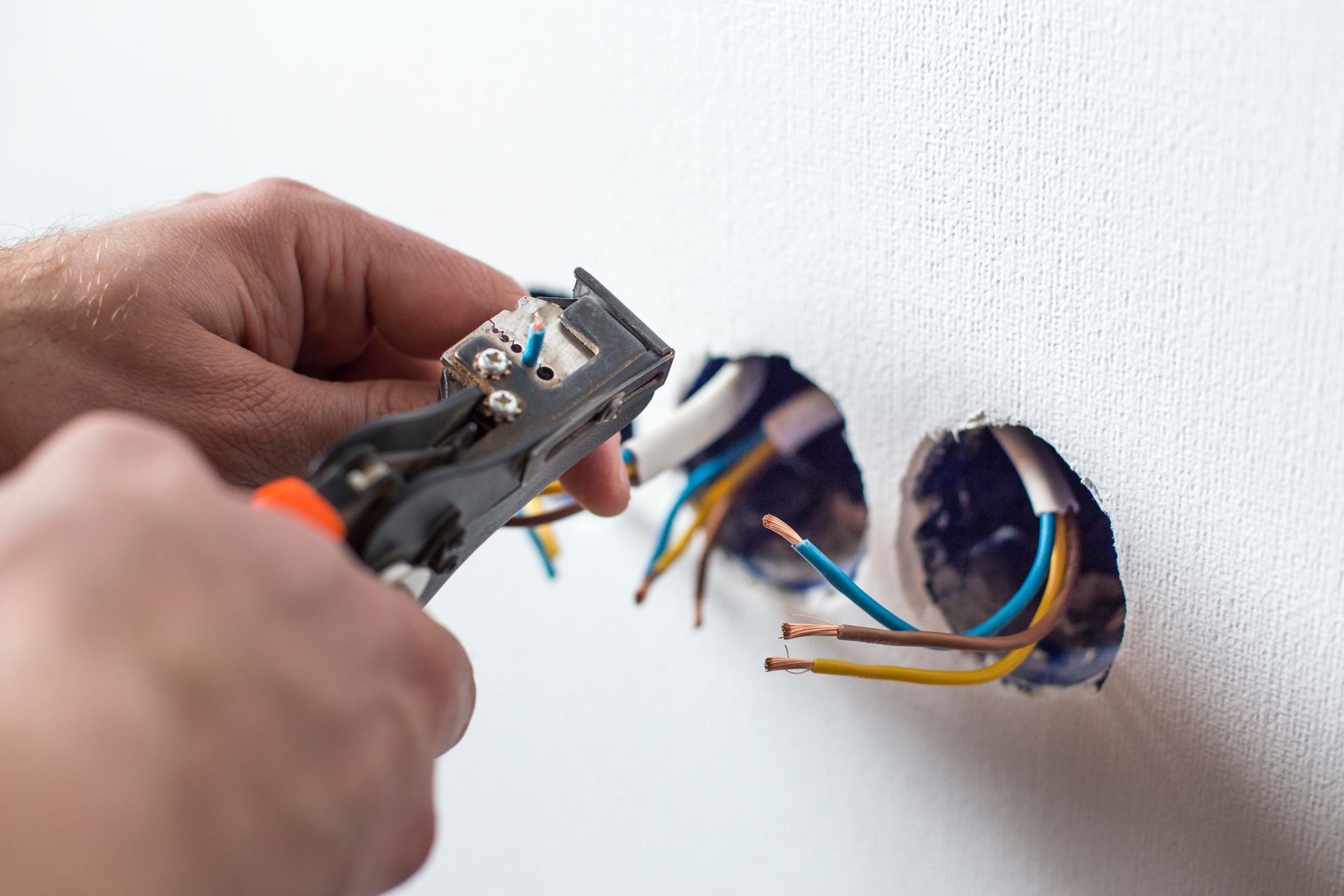 Hand cutting exposed electrical wires in a wall with wire strippers