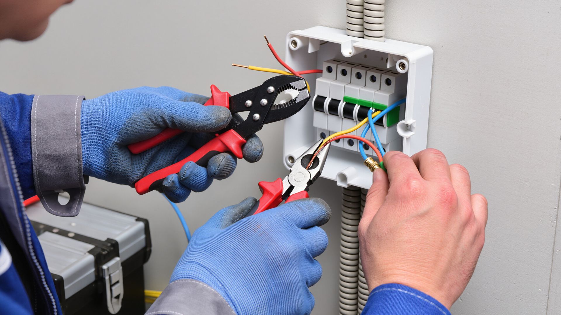 Technicians in blue gloves wiring an electrical panel with pliers and tools