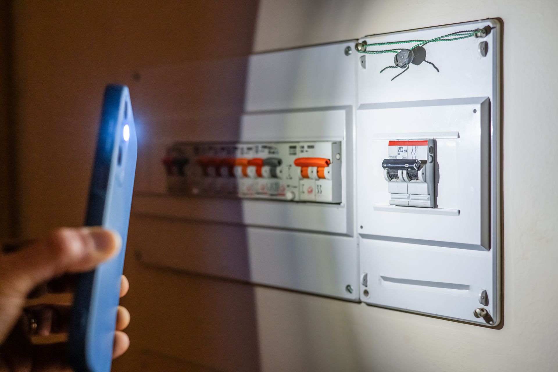 Handheld flashlight illuminating an electrical panel with circuit breakers on a wall