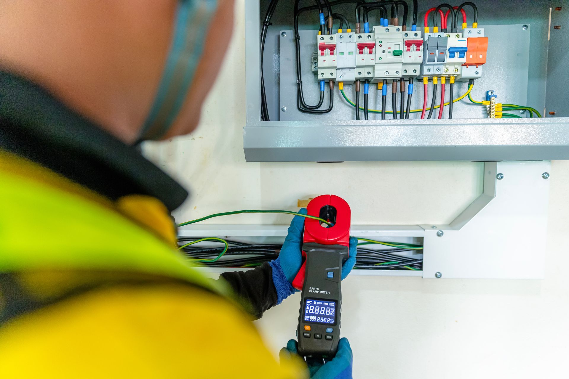 Electrician using a thermal camera to inspect an open electrical panel with colored wiring.