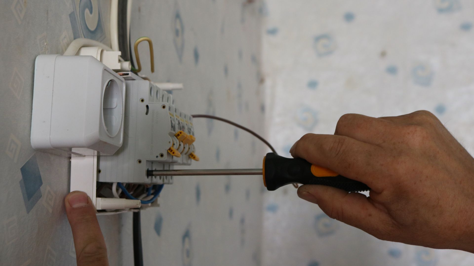 Hand tightening a wall-mounted electrical outlet box with a screwdriver.
