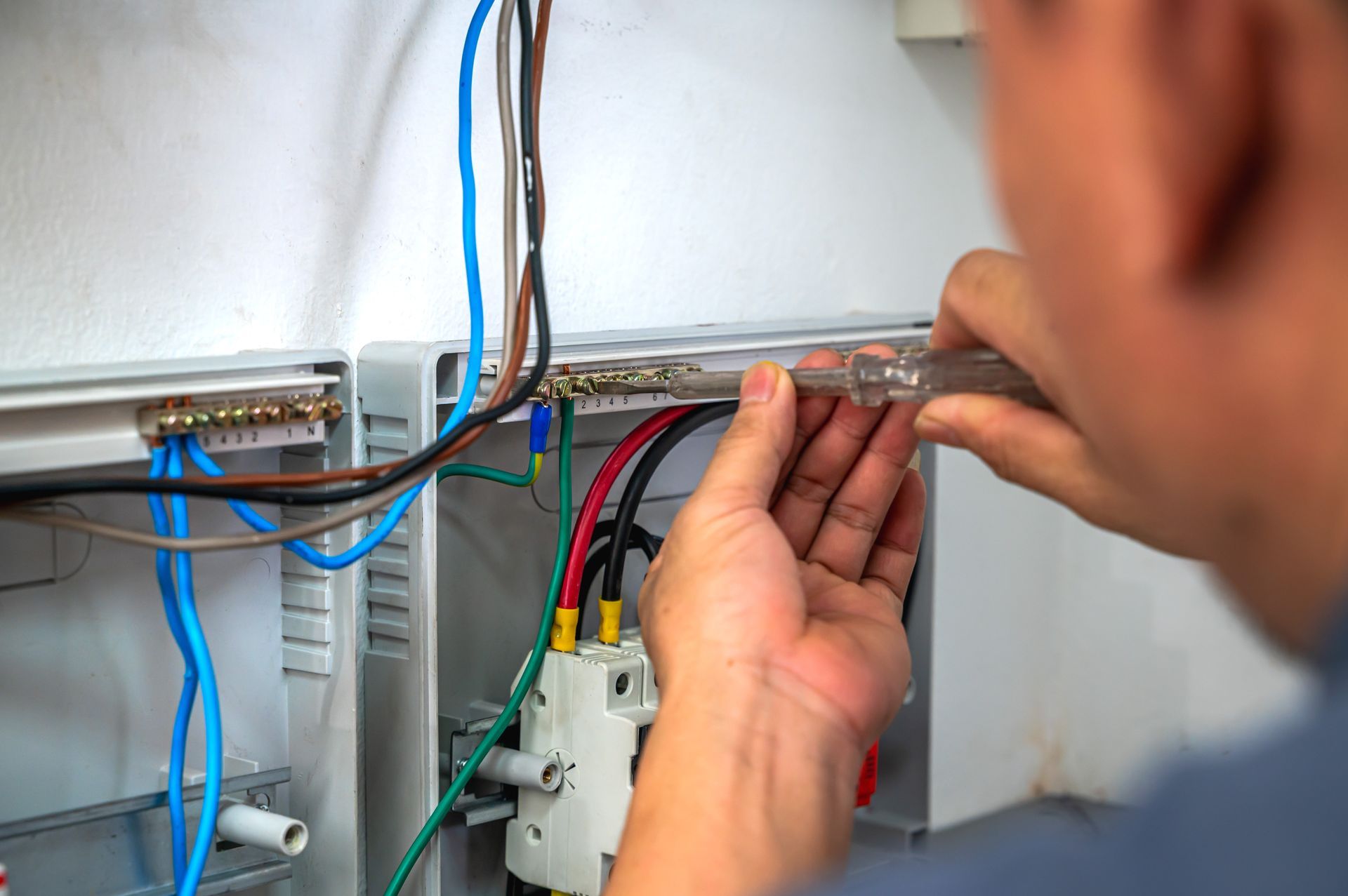 Technician wiring cables in an electrical panel, using a tool near blue and black wires.