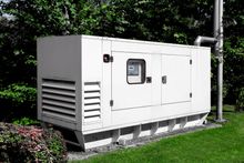 Large white industrial generator unit on a concrete pad beside grass and trees outdoors Large white industrial generator unit on a concrete pad beside grass and trees outdoors