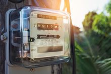Close-up of an outdoor electric meter in a clear plastic box with sunlight and greenery behind it Close-up of an outdoor electric meter in a clear plastic box with sunlight and greenery behind it