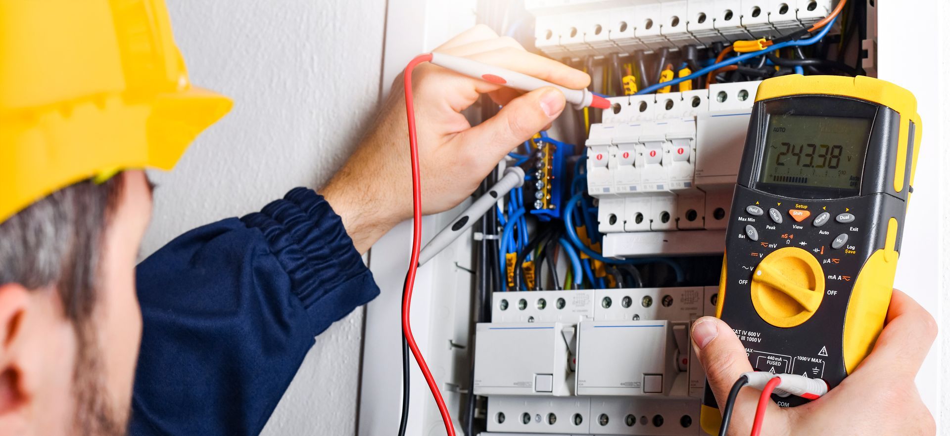 Electrician testing circuit breaker panel with multimeter in an electrical box