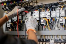 Technician in gloves testing wiring inside an electrical control panel with multicolored cables. Technician in gloves testing wiring inside an electrical control panel with multicolored cables.
