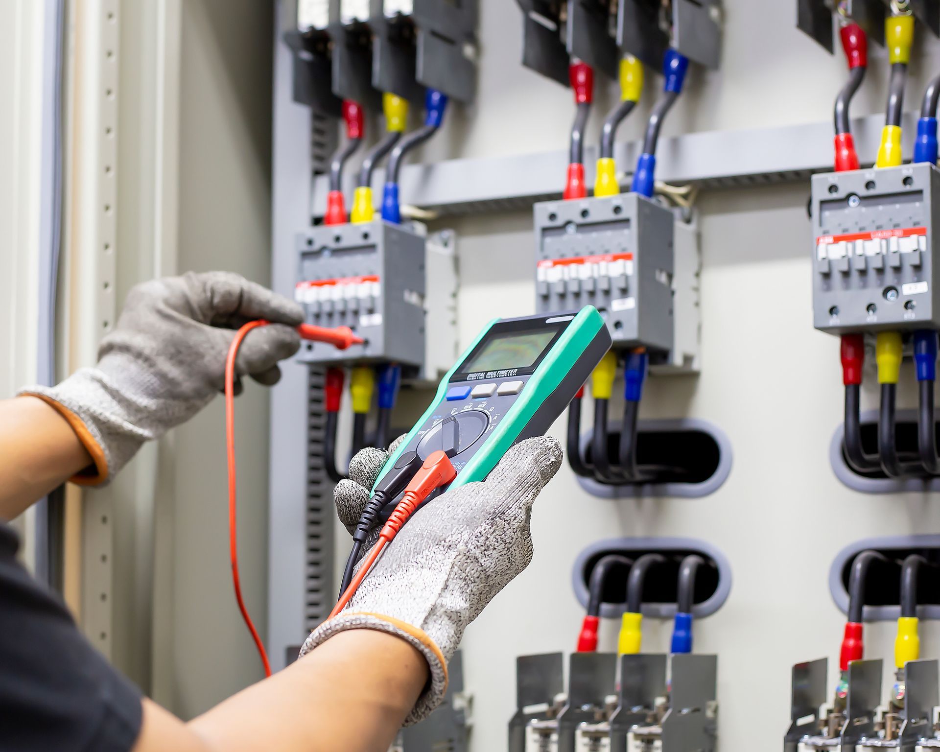 Technician testing electrical control panels with a multimeter in an industrial cabinet