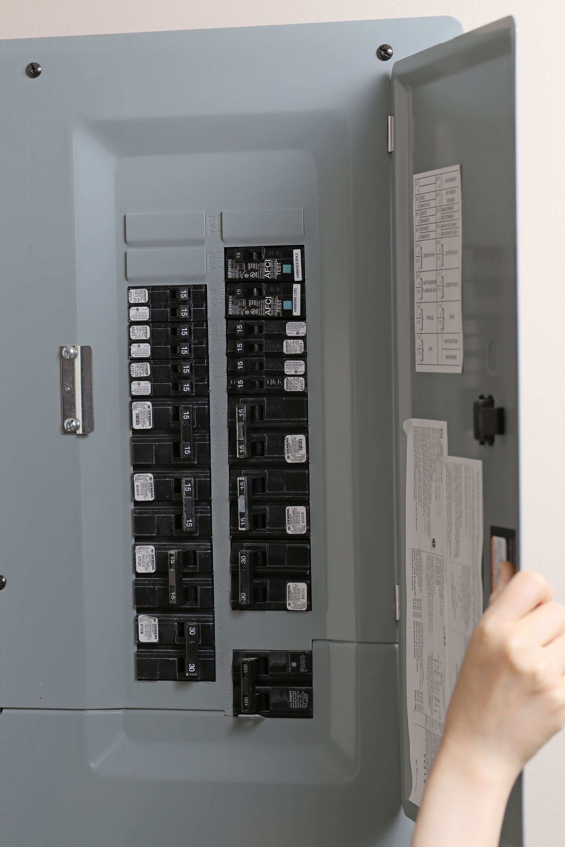 Open electrical breaker panel with a hand opening the door
