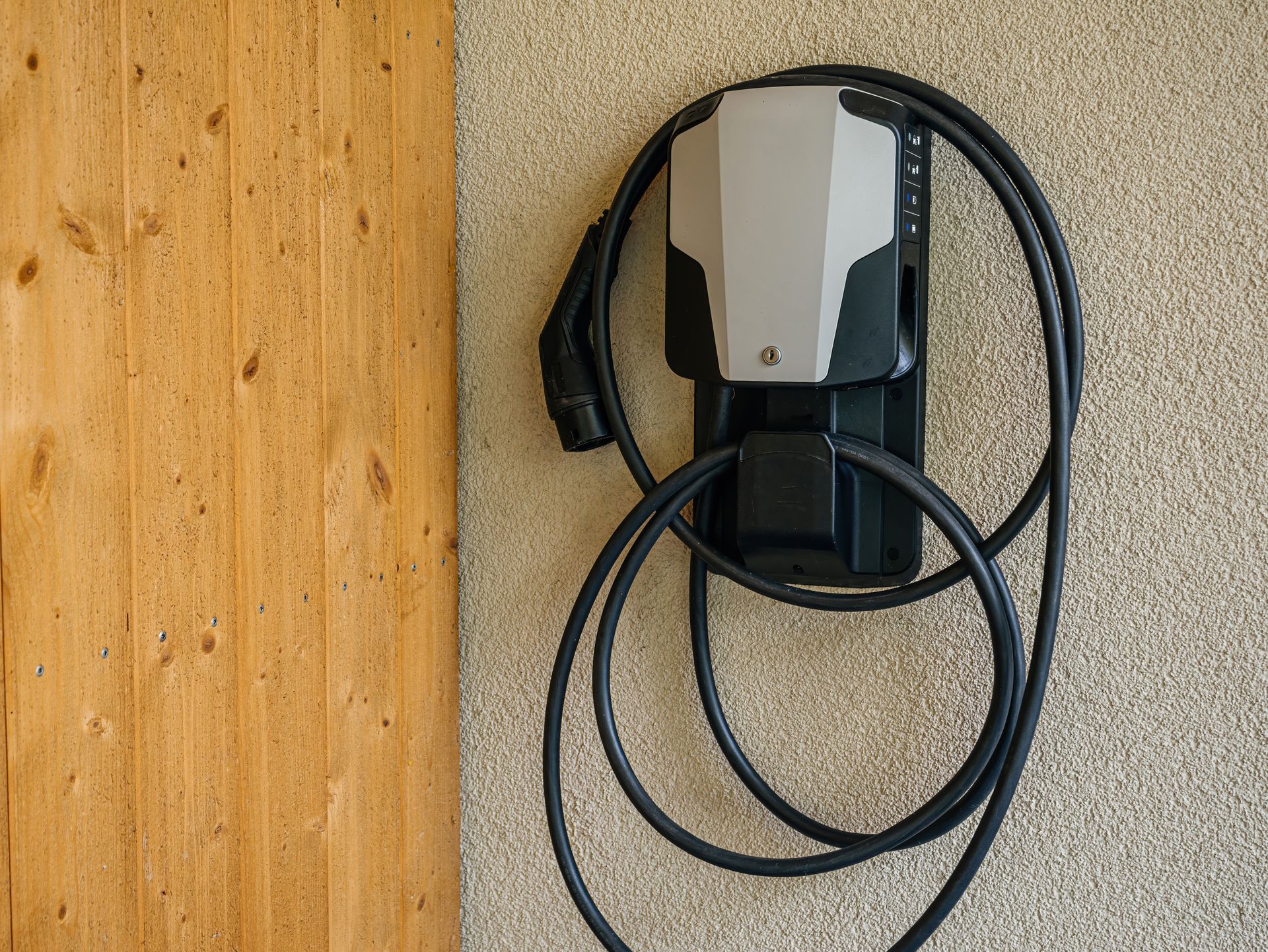 Wall-mounted electric vehicle charging station with coiled cable on a wooden wall