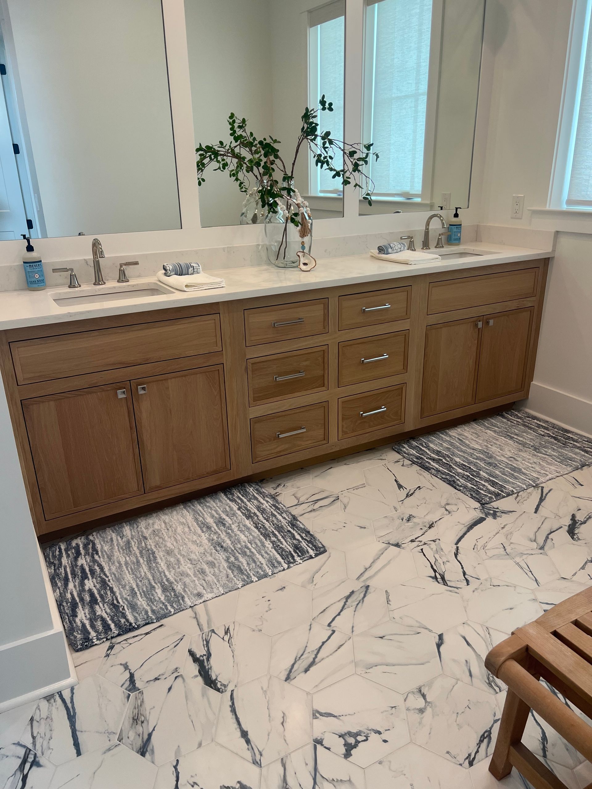 Bathroom with double vanity, light wood cabinets, marble floor, and decorative plants.
