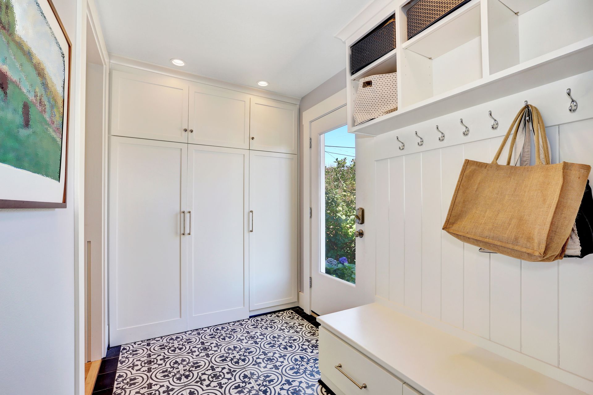 White entryway with storage cabinets, bench, hooks, and patterned floor.