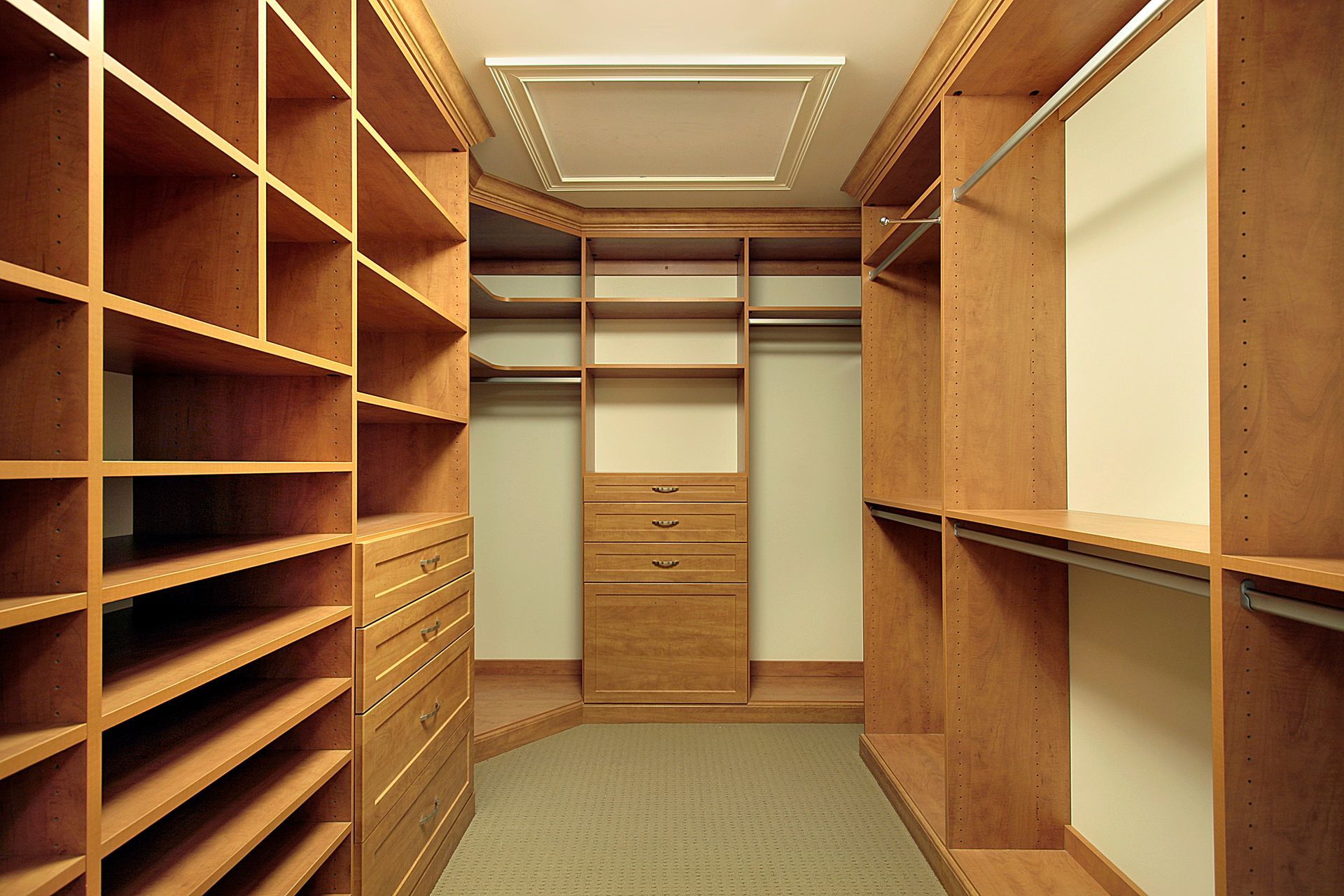 Wooden walk-in closet with shelves and hanging rods. Neutral carpet, beige walls, and recessed lighting.