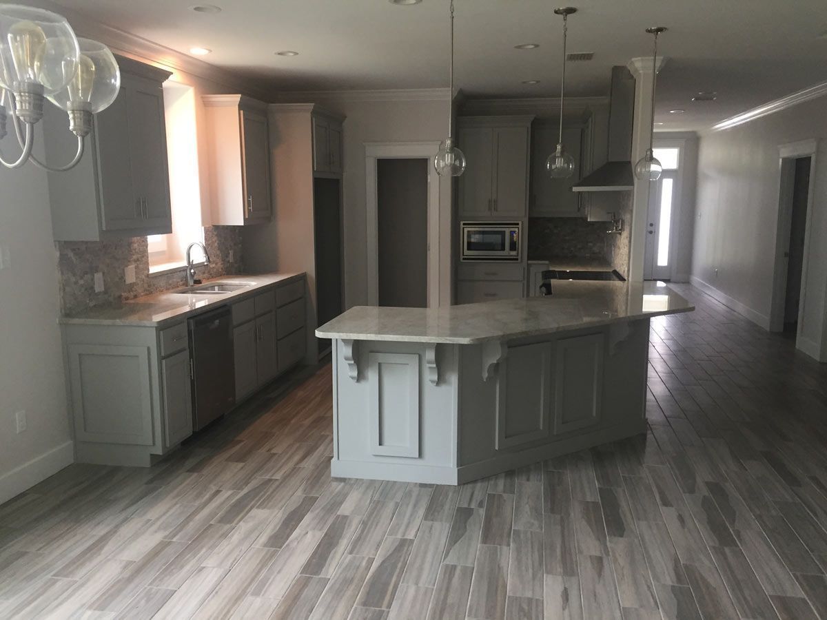 Modern kitchen with gray cabinets, island, and light wood-look flooring.