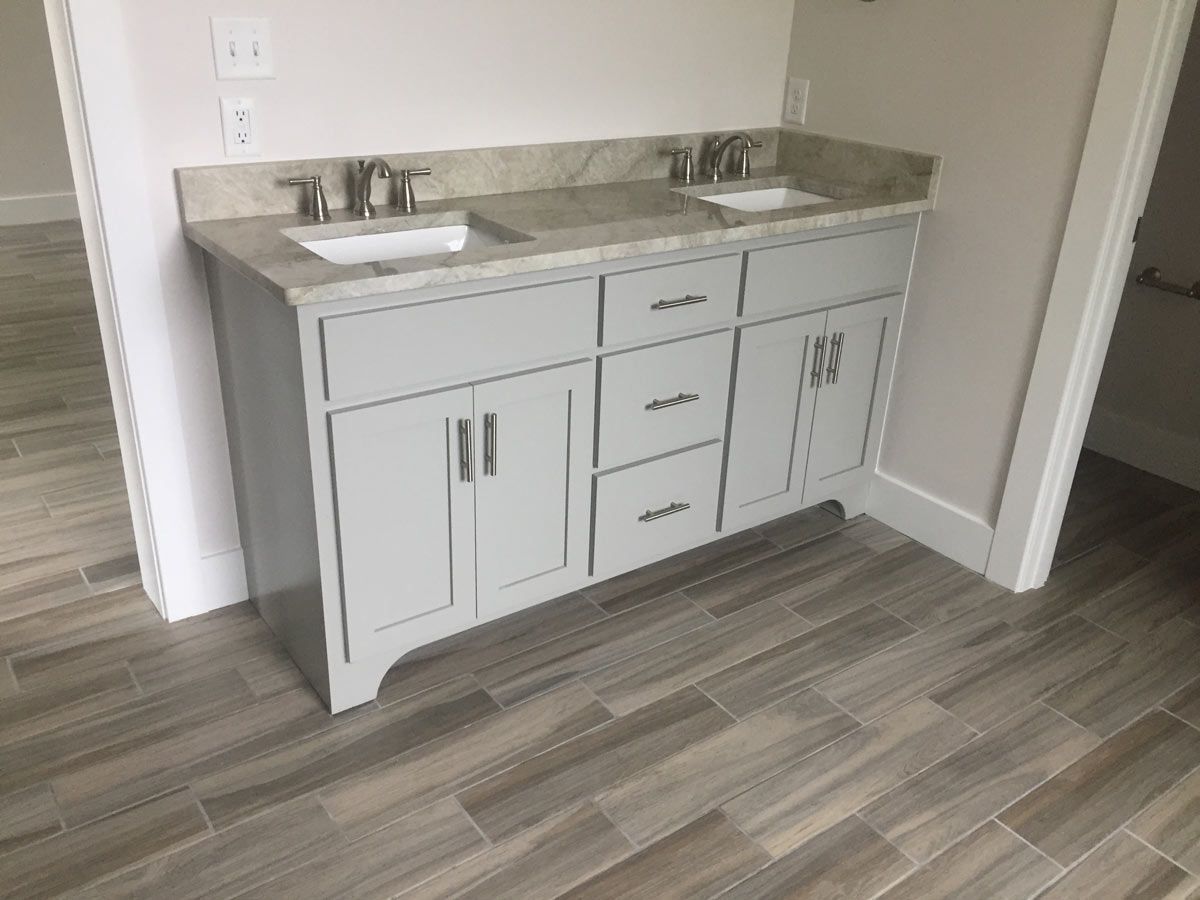 Gray double sink vanity with granite countertop and wood-look tile flooring.