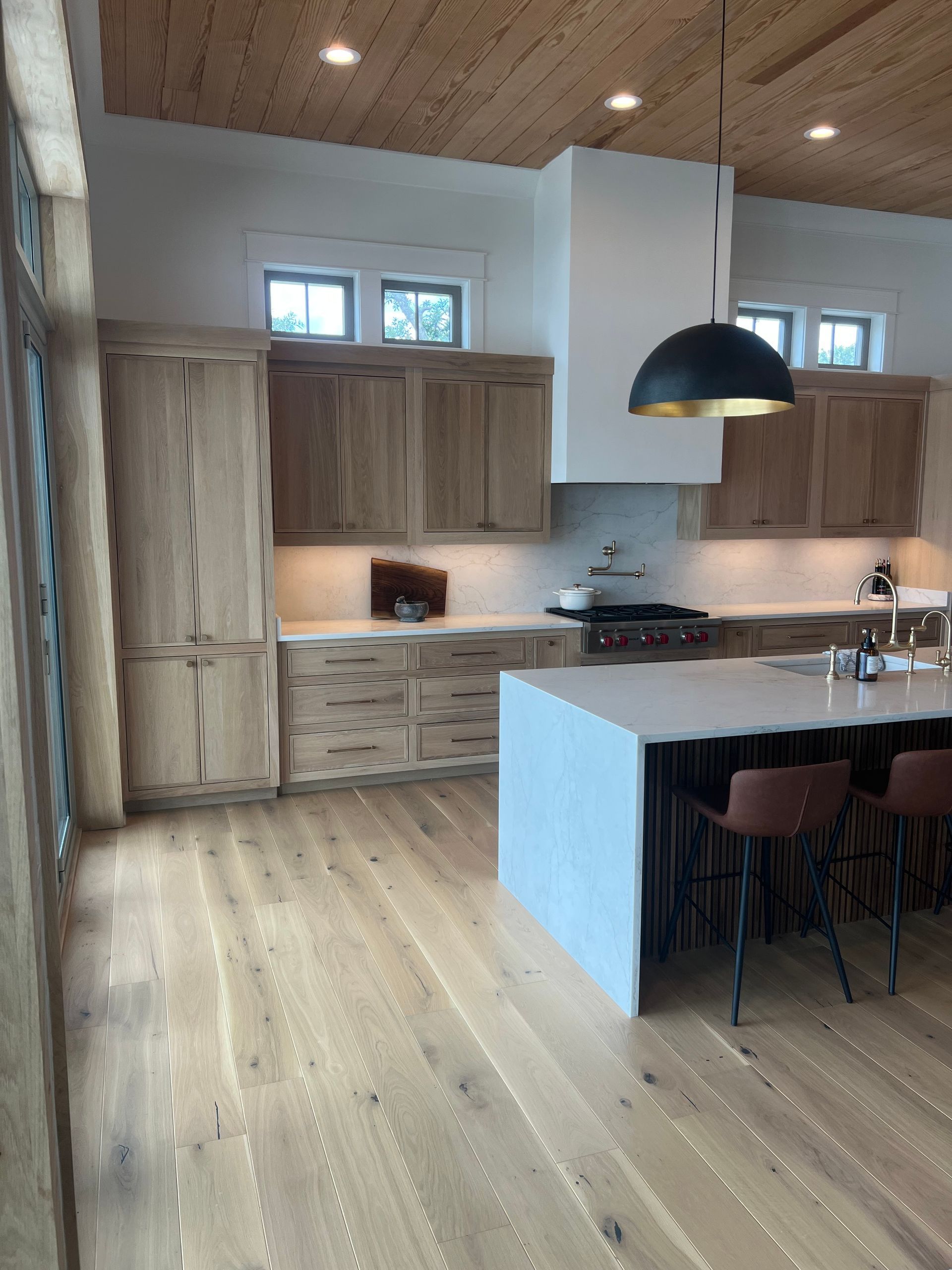 Bright kitchen with light wood cabinets, gray countertops, stainless steel appliances, and wood floors.