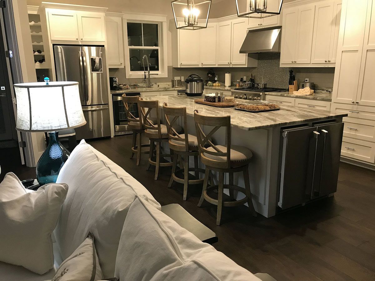 Kitchen with white cabinets, large island with seating, stainless steel appliances, and dark wood flooring.