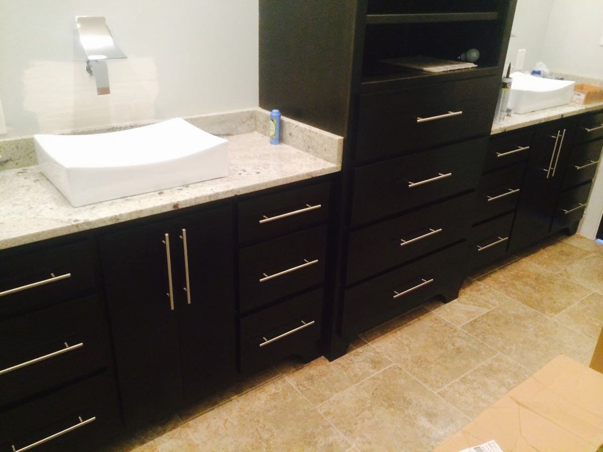 Dark cabinetry with silver hardware, a white sink, and light countertop.