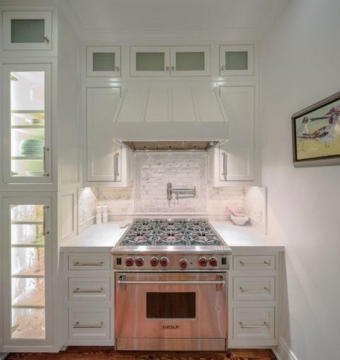 White kitchen with stainless steel oven, cabinets, range hood, and tile backsplash.