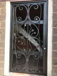 Puerta de hierro forjado negro con ornamentado diseño floral, empotrada en una pared de ladrillo.